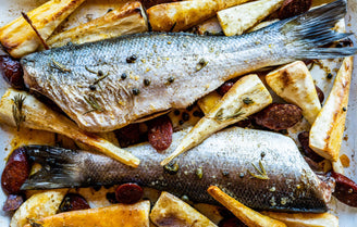 Two whole sea bass on a bed of parsnips and chorizo in a tray.