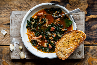 A bowl of Bacon, Kale & Bean Soup with a slice of sourdough toast.