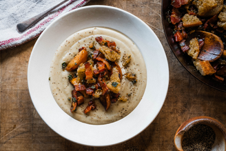 A bowl of Apple & Celeriac Soup with Crispy Bacon, Sourdough & Sage.