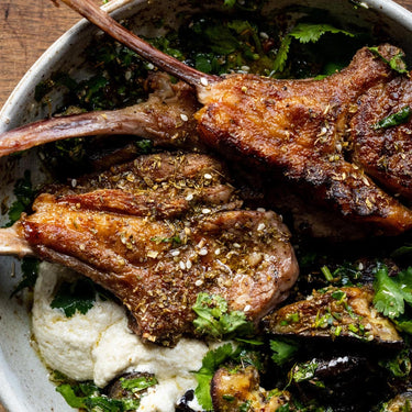 A meal of cooked Grass Fed Lamb Chops with vegetables and herbs.