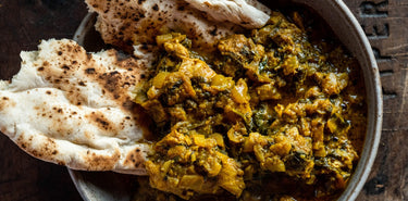 A bowl of Bini's Jammu Chicken Curry Healthy Ready Meal with naan and white rice.
