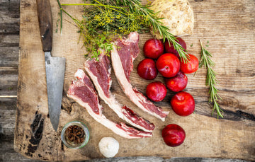 Cull Yaw Mutton Loin Chops on a chopping board with vegetables, herbs and spices.