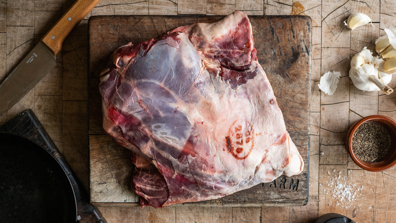 A whole, raw, wild venison shoulder on a chopping board.