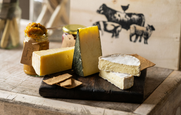 A curated selection of Artisan Cheeses including Tunworth, Cornish Yarg, Quicke’s Vintage Cheddar, with chutney and crackers.