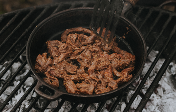 A pan of native breed pork stir fry being cooked over an open flame.