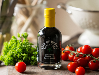 A bottle of Isle of Wight, Oak Smoked Tomato Balsamic Vinegar with tomatoes and parsley.