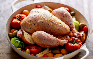 A whole, raw. 100% pastured properly free range chicken on a bed of tomatoes, garlic, onion, and seasonings.