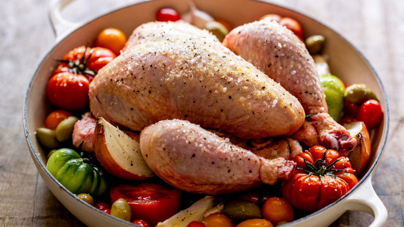 A whole, raw. 100% pastured properly free range chicken on a bed of tomatoes, garlic, onion, and seasonings.