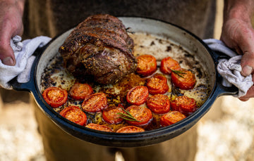 A man holding a pan of cooked Cull Yaw Mutton Rump with tomatoes and herbs.