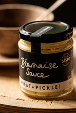 Jar of Béarnaise Sauce from 'What a Pickle!' on a wooden surface with a spoon and bowl in the background.