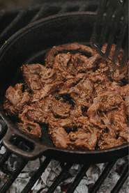 A pan of native breed pork stir fry being cooked over an open flame.