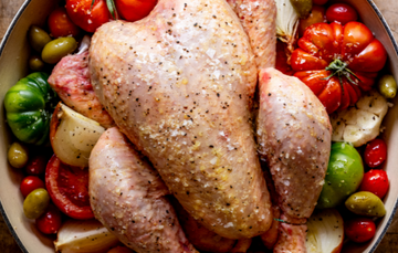 A whole, raw. 100% pastured properly free range chicken on a bed of tomatoes, garlic, onion, and seasonings.