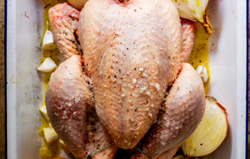 A whole, raw 100% pastured properly free range chicken on a bed of onions, garlic, and seasonings.