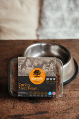 Benyfit Turkey Meat Feast pet food packaging on a wooden surface with a metal bowl in the background.