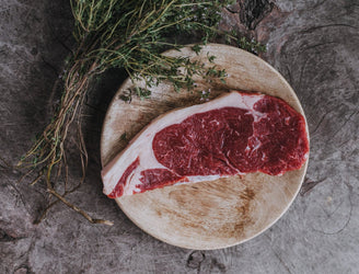 A raw, Grass Fed Beef Sirloin Steak with a bunch of thyme.