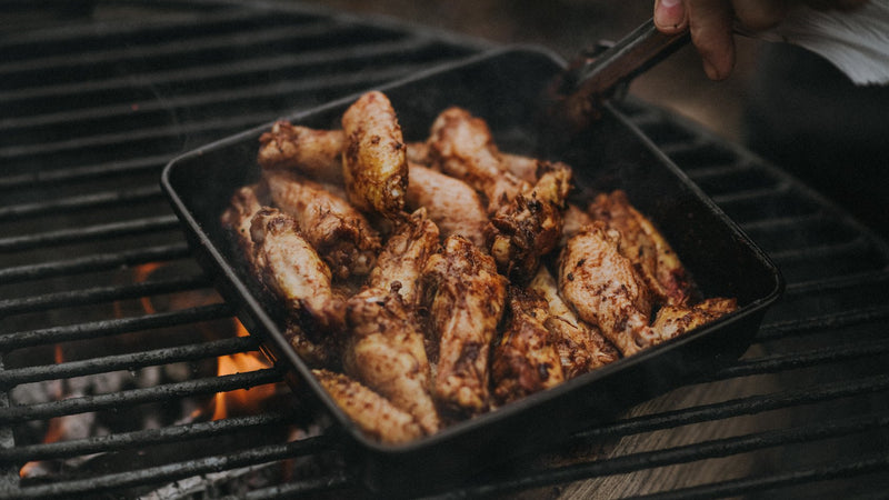 Marinated properly free range chicken wings cooking in a pan on a barbecue.