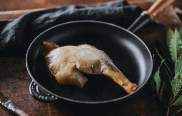 A properly free range confit goose leg cooking in a pan with bay leaves