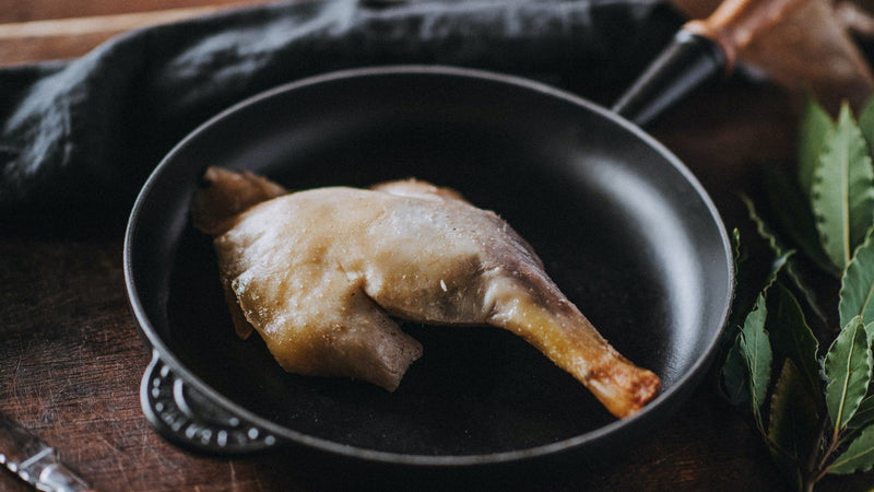 A properly free range confit goose leg cooking in a pan with bay leaves