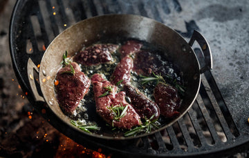 Grass fed lamb's liver cooking in a pan over a barbecue with fresh rosemary