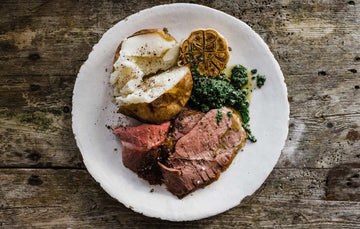 A meal of cooked, grass fed, cull yaw leg of mutton with a baked potato, roasted garlic, and parsley sauce.