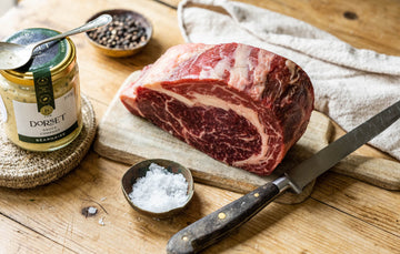 A raw, grass fed beef ribeye sharing steak, salt and pepper, and a jar of Bearnaise sauce from The Dorset Sauce Company.