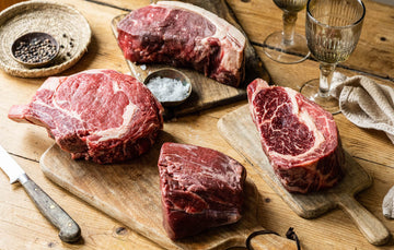 A selection of raw, grass fed beef ribeye sharing steaks with salt and pepper.