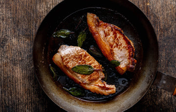 Native breed pork loin steaks cooking in a pan with herbs