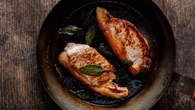 Native breed pork loin steaks cooking in a pan with herbs