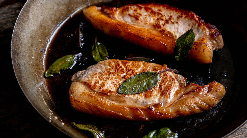 Native breed pork loin steaks cooking in a pan with herbs