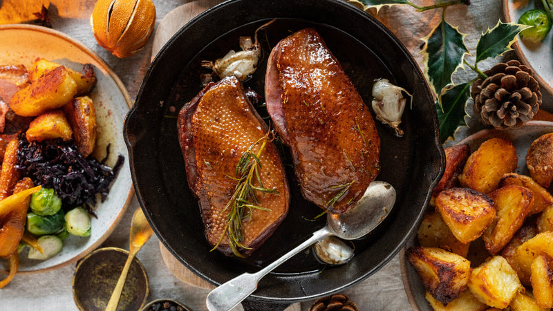 A roast dinner spread with potatoes, goose breasts, and vegetables.
