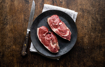 A pair of raw grass fed lamb rump steaks on a plate.