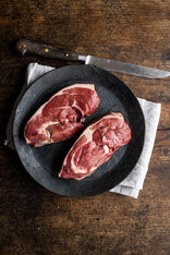 A pair of raw grass fed lamb rump steaks on a plate.