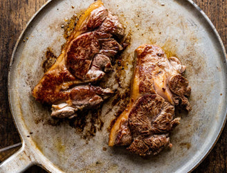 A pair of raw grass fed lamb rump steaks on a plate.