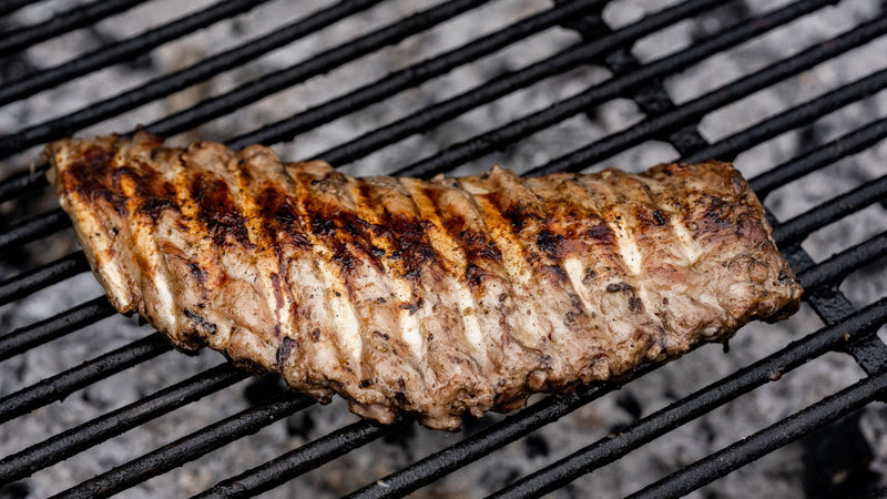 A rack of native breed pork ribs cooking on a barbecue