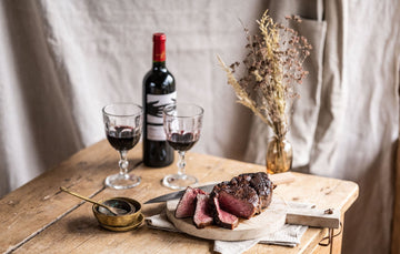A cooked and sliced grass fed beef ribeye sharing steak with glasses of red wine.