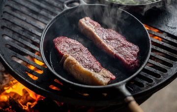 A pair of Grass Fed Beef Sirloin Steaks cooking in a pan over an open flame.