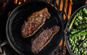 A pair of cooked Grass Fed Beef Sirloin Steaks with peas and asparagus.