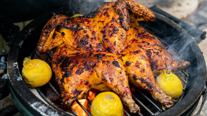A whole, properly free range spatchcock chicken cooking on a barbecue with lemons