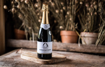 A bottle of Swanaford Classic Cuvée sparkling wine standing on a chopping board.