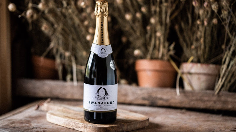 A bottle of Swanaford Classic Cuvée sparkling wine standing on a chopping board.