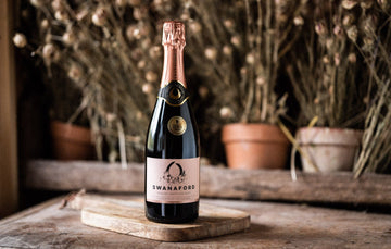 A bottle of Swanaford Brut Rosé sparkling wine standing on a chopping board.