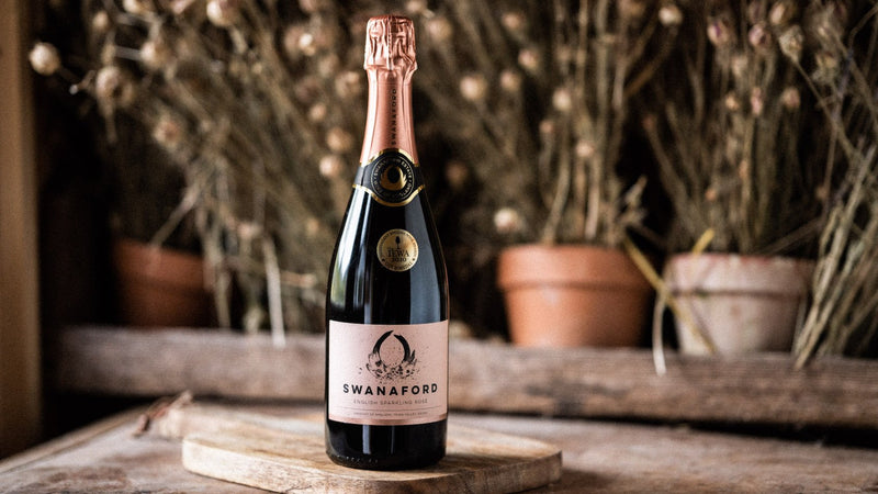 A bottle of Swanaford Brut Rosé sparkling wine standing on a chopping board.