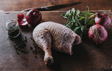 A raw Properly Free Range Turkey Leg with onions, herbs and peppercorns