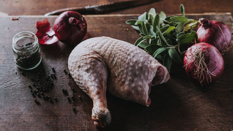 A raw Properly Free Range Turkey Leg with onions, herbs and peppercorns