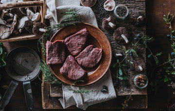 Raw wild venison steaks with mushrooms and fresh herbs