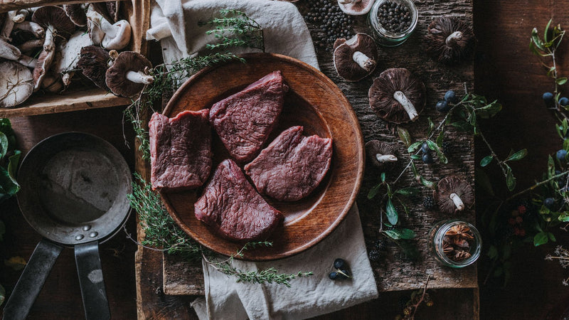Raw wild venison steaks with mushrooms and fresh herbs