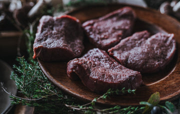 Raw wild venison steaks with mushrooms and fresh herbs