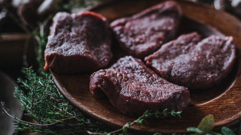 Raw wild venison steaks with mushrooms and fresh herbs